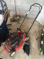 Angled view of mower on concrete floor showing deck, engine cover, handle and side chute on floor