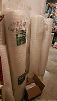 Photo of several white foam underlayment rolls wrapped in plastic with QuickStyle labels, standing vertically in basement area.