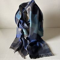 Scarf displayed hanging to show its length, texture, and coloration of blue and gray squares.