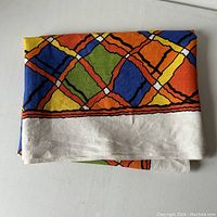 Folded 100% linen table cloth showing colorful geometric pattern and natural linen border.