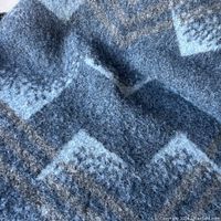 Close up of geometric pattern and texture of the wool blanket in assorted blue and gray tones.