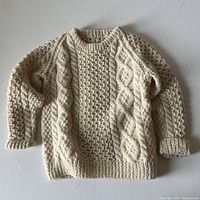 Full view of child's wool hand knit sweater laid flat on a light surface showing cable and textured knit patterns.