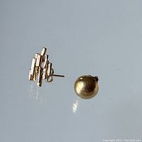 Pair of gold stud earrings, one half-round screw-post and one Brutalist style tri-color gold design, displayed against a reflective surface.