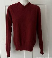 Front view of red cashmere V-neck sweater on mannequin, showing knit texture and ribbed cuffs and hem.