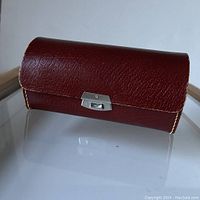 Angled front view of brown leather rectangular case with metal clasp closed.