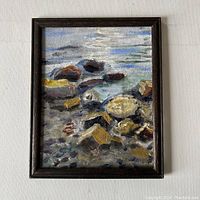 Full view of the original oil painting in dark wood frame depicting lake shore with rocks and water.