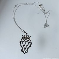 Full view of the necklace showing the chain laid out and the pendant that features two hearts under a crown.