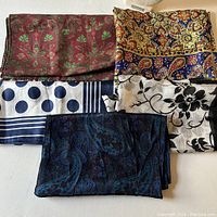 Five scarves with different patterns and colors shown on a flat surface