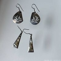 Pair of sterling silver cut-out earrings with leaf motifs and pair of triangular mother of pearl inlay earrings on white background.