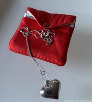 Sterling silver heart pendant placed on top of a red jewelry pouch showing the pendant and chain clasp
