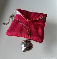 Heart-shaped sterling silver pendant with etched details resting on a red fabric jewelry pouch.