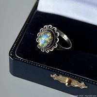 Front side view of sterling silver ring with scalloped bezel and a round iridescent stone showing green, black, and gold inclusions.