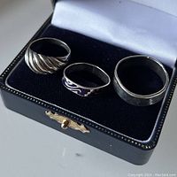 Rings in a black velvet ring box with white satin lining, showing all three rings side by side.