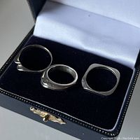 Three sterling silver stack rings displayed on a black cushioned jewelry box lid, showing twist, rounded, and square bands.