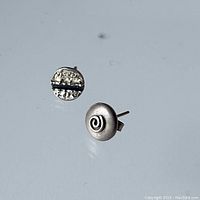 Close-up image showing front and back of two different sterling silver stud earrings, one with spiral design, the other textured with black line detail.