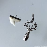 Sterling silver buck pendant and shark's tooth pendant shown together on a reflective surface