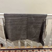 Suede cowhide leather hide draped over a railing showing smooth texture and smokey grey color.