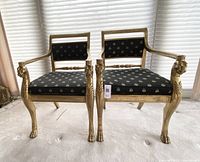 Frontal view of two gilded chairs side by side showing carved lion head armrests and brocade upholstery pattern.