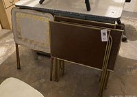 Four folding TV trays stacked together showing various tops and metal legs, with some rust and wear