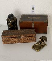 Front and angled view showing all four items: wooden humidor box with painted design, carved wooden box, black decorative tin with gold floral design, and brass ashtray with squirrel figurine.