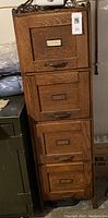 Front view of the antique wood file cabinet showing four drawers, each with metal handle and label holder.