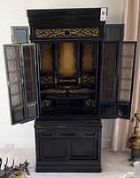 Front of Asian shrine cabinet with doors open showing intricate carved woodwork and gold background inside.