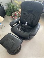 Front view of black leather recliner chair and matching ottoman on carpeted floor