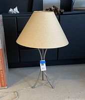 Full view of iron base table lamp with beige parchment lampshade showing rip damage.