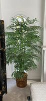 Tall artificial bamboo tree with long green leaves in woven basket against arched window