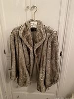 Photo of light gray vintage fur coat hanging on a wooden hanger with label 'Gibson'