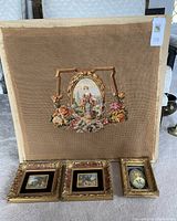 Overall lot showing the finished needlepoint canvas with a Victorian lady surrounded by a floral and ornate frame, and three ornate gold framed miniature paintings, two landscapes and one portrait.