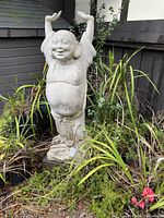 Photo of the large laughing Buddha statue showing damage and cracks, surrounded by plants.