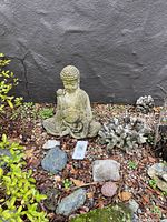 Photo showing the Buddha statue seated amongst garden stones, natural coral pieces, and surrounding plants, illustrating condition and scale.