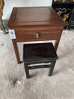 Pair of side tables, larger reddish wood table with drawer and smaller black table, both solid wood.