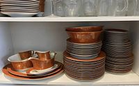 Photo of stacked plates, bowls, cups, and other serving pieces featuring orange and gold floral design.