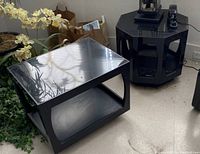 Two black wood glass topped side tables: one rectangular with bottom shelf, one octagonal with bottom shelf