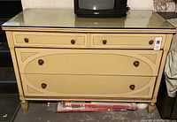 Front view of vintage yellow low dresser with two small top drawers and two larger bottom drawers, round knob pulls, and glass top.