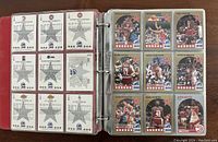 Photo showing an open binder with 1990 NBA Hoops cards displayed in plastic sleeves, front and back view of cards visible.