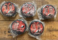 Front view of five sealed hockey pucks with team players printed on top in red and black with Canadian maple leaf logo