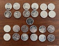 Full view of all 25 Canadian quarters arranged in 5 rows on wood background showing the different designs from the Millennium series 2000.
