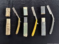 Three vintage straight razors with original cases laid on black background, showing wear on cases and metal blades with varied handle patterns.
