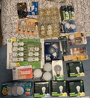 Full overview of the lot showing a large assortment of lightbulbs in original packaging and loose bulbs on a patterned fabric background.
