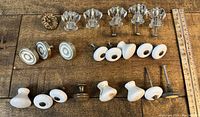 Photo showing 22 assorted drawer knobs of varying materials: clear glass, ceramic, and metal, arranged next to a ruler for scale.
