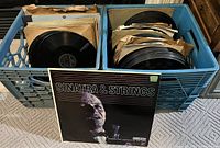 Two blue plastic milk crates filled with vintage 78 RPM records mostly in paper sleeves. One crate shows a visible album 'Sinatra & Strings' leaning outside the crate.