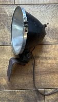 Side view of vintage King Bee automotive lamp showing black conical metal housing, chrome rim, attached rusty mounting bracket, and original wiring
