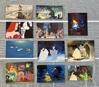Eleven official Disney postcards laid out flat on gray fabric surface, each showing vibrant colorful classic Disney animation scenes.