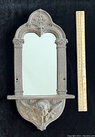 Front view of cast iron angel wall mirror with ruler for size reference showing 14 x 8 inches dimensions