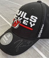 Black New Jersey Devils hockey cap with Reebok sticker and Taylor Hall signature on brim, showing side view with branding and signature.