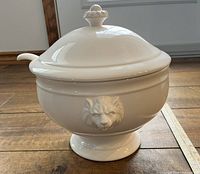 Front view of white ceramic serving bowl with lionshead detail and sitting lid with knob.