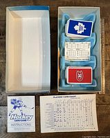 Open game box with visible decks of cards, blue plastic insert, and stack of scorecards